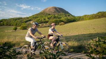 Two cyclists on a dirt path with a hill and trees in the background.