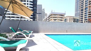 A rooftop pool area with lounge chairs and a large umbrella, surrounded by high-rise buildings.