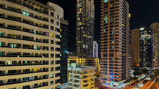 A nighttime cityscape with high-rise buildings, a busy street, and illuminated signage.