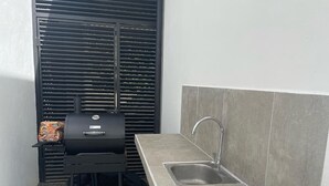 Eine kleine Küchenzeile mit integriertem Spülbecken, einem Grill und einem Fenster mit Jalousien.