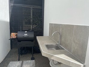 Une petite cuisine équipée avec un évier intégré, un barbecue et une fenêtre avec des stores.
