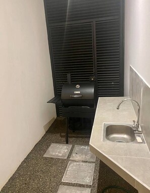 Una cocina compacta con una parrilla integrada, un lavamanos y piso de baldosas.