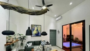 A modern living room with a wooden coffee table, a sofa, a dining table, pendant lights, a ceiling fan, and a sliding glass door leading to a pool area. - House with private pool and fully equipped BBQ (Jaco)