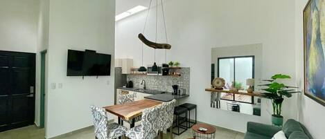 Cozinha moderna com área de jantar, um sofá e televisão fixada na parede.