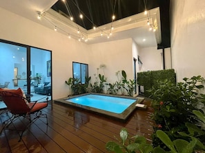 A modern indoor pool area with a wooden deck, a red chair, and potted plants.