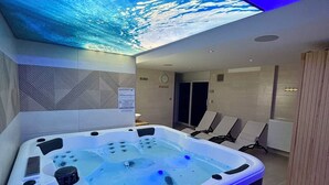 Un baño moderno con una bañera grande, un techo con cascada y una zona de estar con sillas.