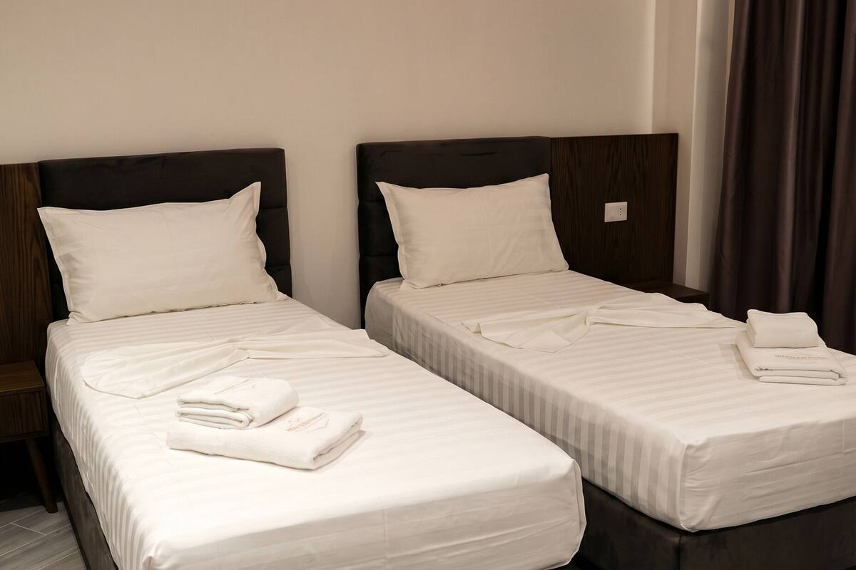 Two single beds with white linens and folded towels, a dark headboard, and a wooden nightstand.