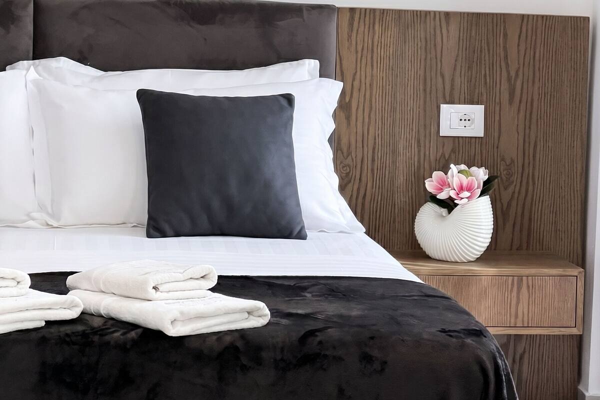 A neatly made bed with a black headboard, white and dark pillows, and folded towels on the bed.