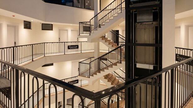 Een ruim interieur met een centrale trap, een glazen dak en een bord dat een locatie aangeeft.