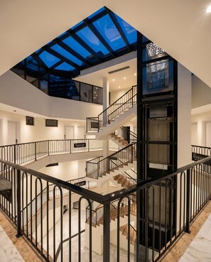 Un intérieur spacieux avec un escalier central, une verrière et un panneau indiquant l’emplacement.