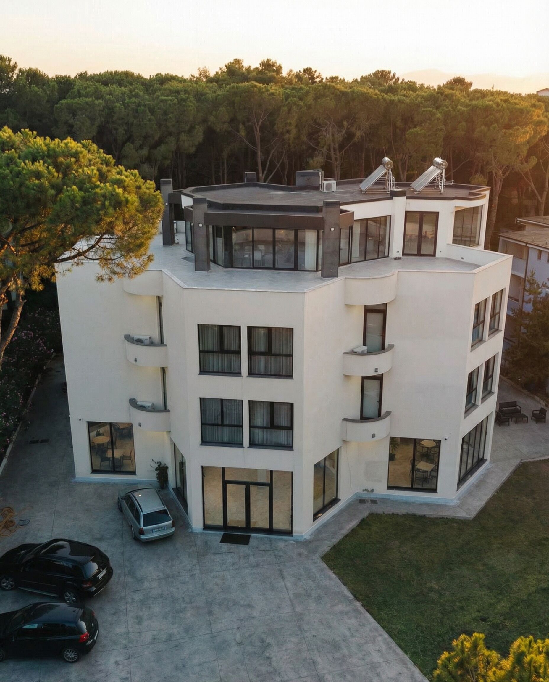 A modern multi-story building with a flat roof, large windows, and a carport.