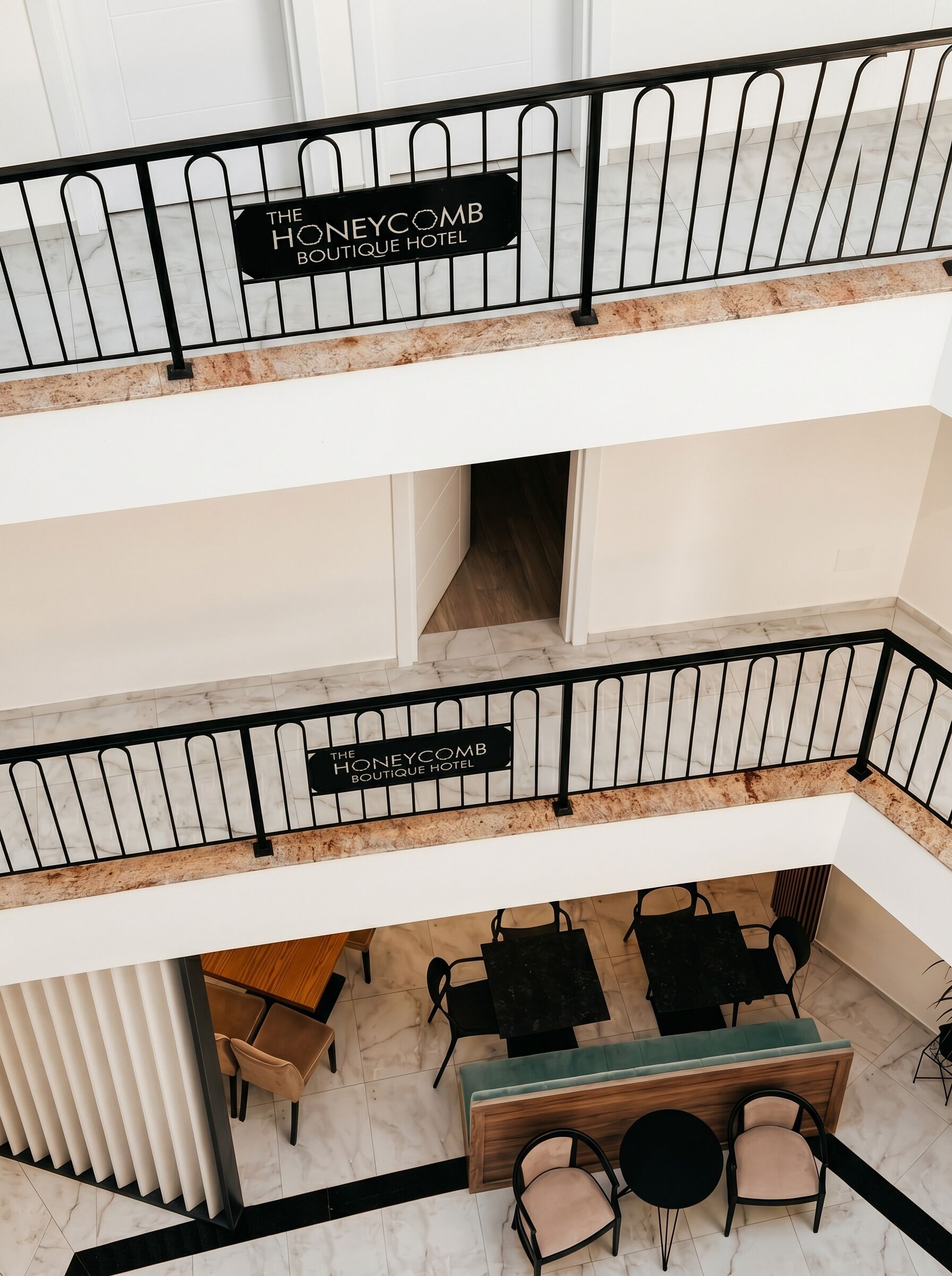 Interior de un hotel de varios niveles con un cartel que dice 'The Honeycomb Boutique Hotel' en la barandilla, una zona de recepción con mesas y sillas, y un diseño moderno con suelo de mármol.