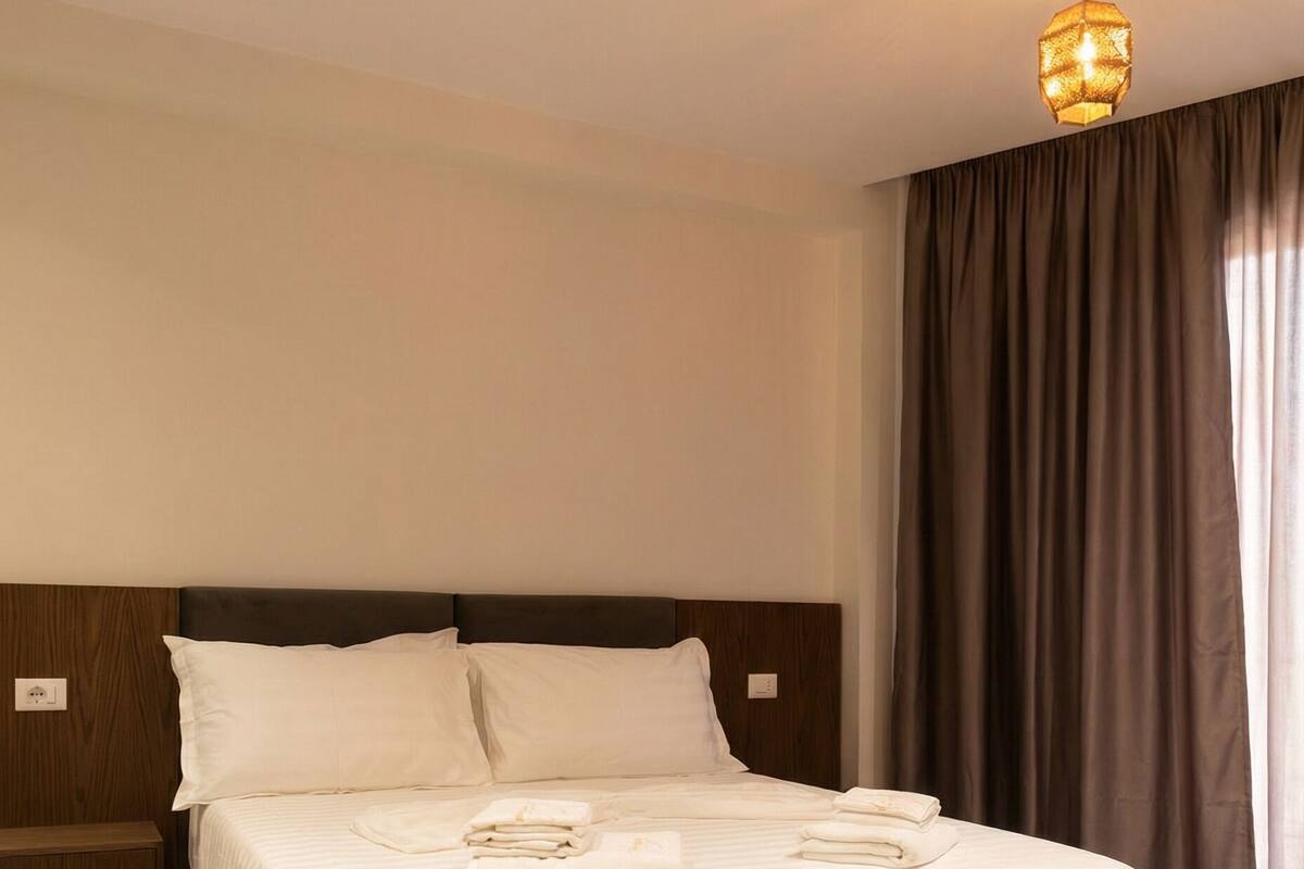 A neatly made bed with white linens and towels, a wooden headboard, and a hanging light fixture.