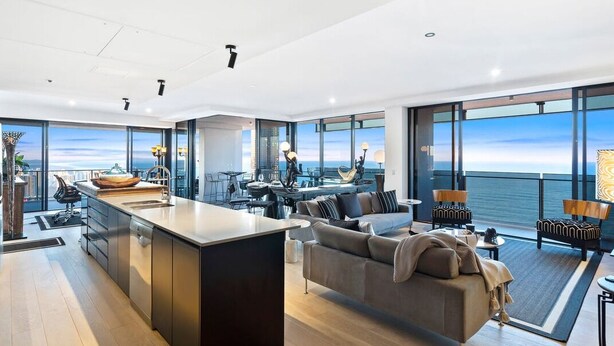 A modern interior with a kitchen island, seating area, and large windows offering ocean views.