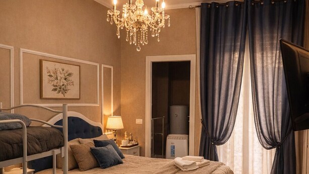 Una habitación de hotel con literas, un candelabro, un televisor, un baño y un ventanal con cortinas.