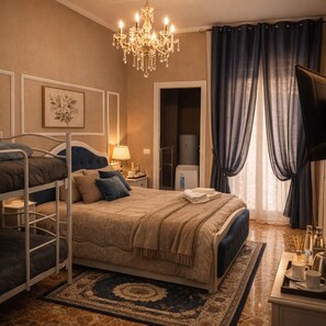 A hotel room with a bunk bed, a chandelier, a television, a bathroom, and a large window with curtains. - Il Castello di Venere (Rota d'Imagna)