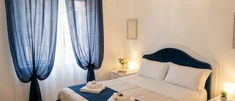 Habitación de hotel con cama, mesita de noche, candelabro y ventana con cortinas.