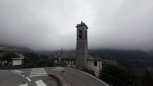 Una iglesia con un campanario, rodeada por un paisaje montañoso y un cielo nublado.