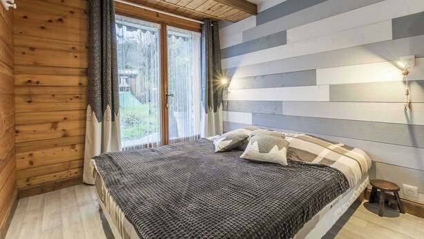 Ein Schlafzimmer mit Holzboden, einem Bett mit gestreifter Bettdecke, zwei Kissen und einem Nachttisch.
