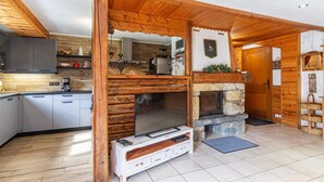 Ein gemütliches Interieur im Chalet-Stil mit Kamin aus Stein, Holzbalken und Küchenbereich.