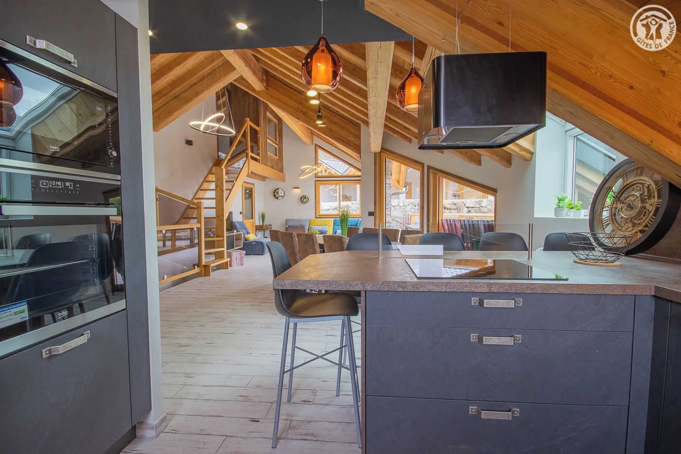 A modern kitchen with a built-in oven, a large island with bar stools, and a rustic wooden ceiling.