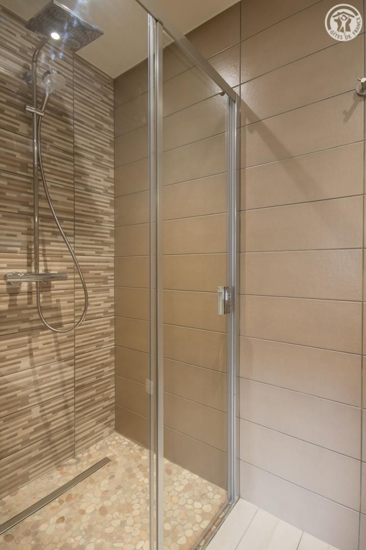 A modern shower with a glass door, a showerhead, and a tiled floor.