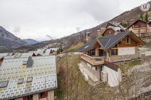 A mountain lodge with a wooden exterior, a balcony, and a view of the surrounding mountains.