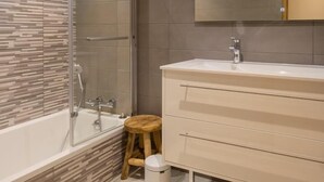 Et moderne badeværelse med bruseniche i glas, et hvidt toiletbord med spejl og flisegulv.