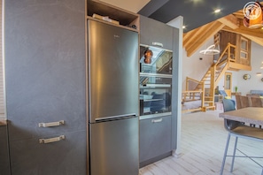 A modern kitchen with a built-in stainless steel refrigerator, oven, and microwave. There is a wooden staircase leading to an upper level.