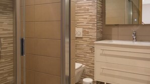 Et moderne badeværelse med brusekabine i glas, toilet og vaskebord med spejl.
