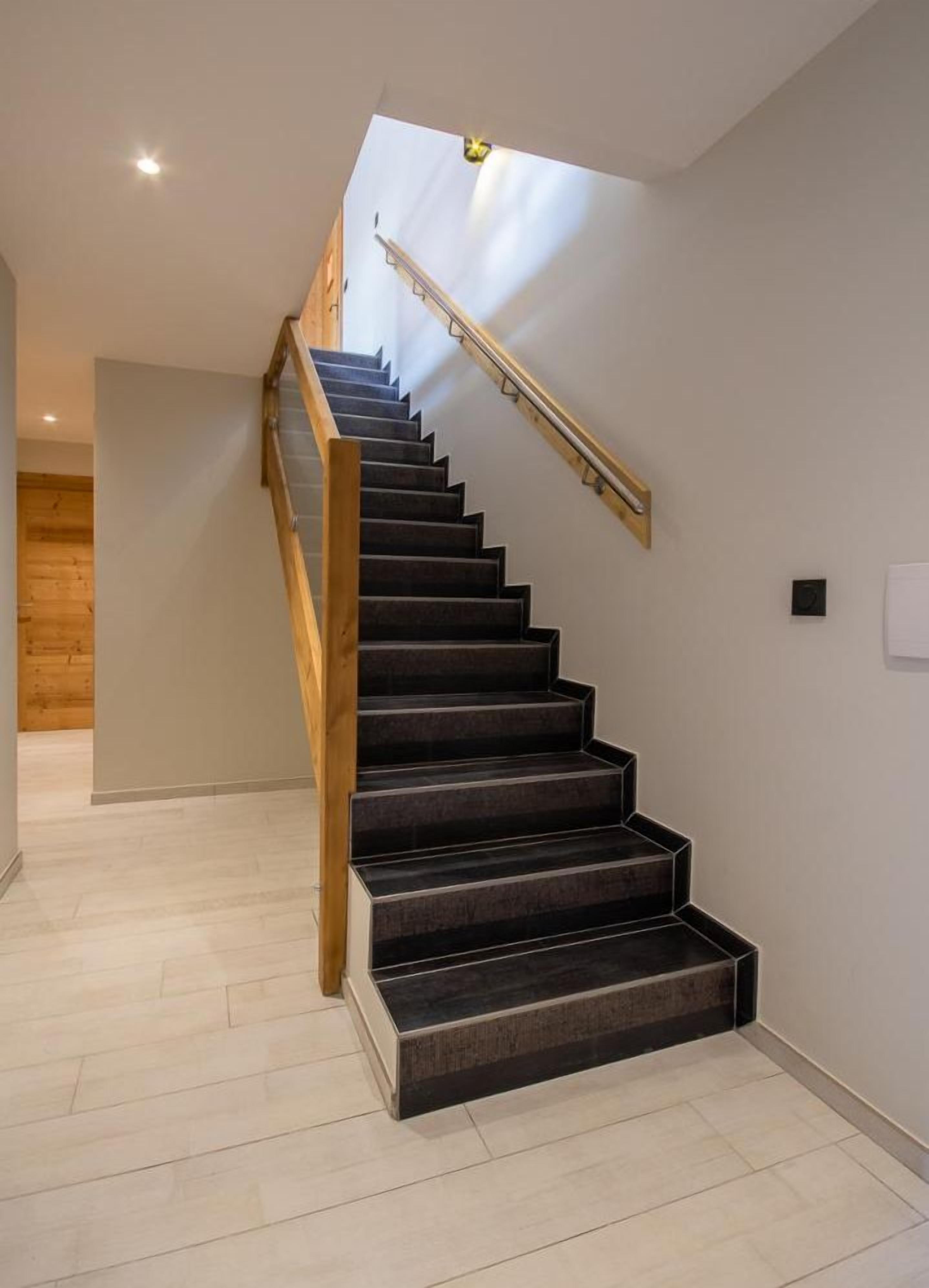 A modern staircase with wooden handrails and dark steps, leading to a room with a wooden door and a light-colored floor.