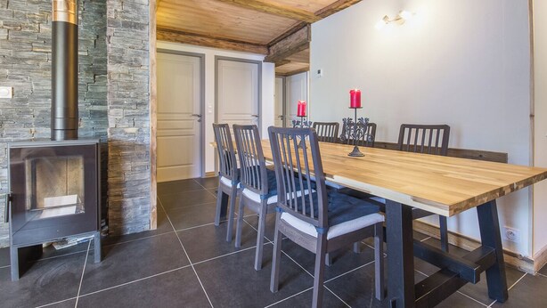 Un comedor con mesa y sillas de madera, una pared de piedra y un estufa de leña.