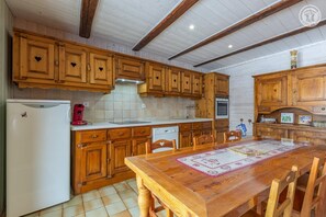 Una cocina con armarios de madera, un refrigerador blanco, una cafetera roja y una mesa de comedor con sillas.