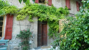 Un edificio rustico con facciata in pietra, persiane rosse e una porta in legno.