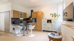 Una cucina moderna con mobili in legno, forno a incasso, macchina del caffè e lavatrice. Ci sono due sgabelli bianchi e un piccolo tavolo rotondo con libri e un bicchiere.