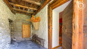 A rustic stone-walled room with a wooden door, a bench, and a basket of flowers.