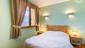 A bedroom with a bed, a window with curtains, two bedside lamps, and a wooden headboard.