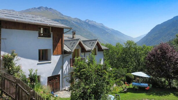 A traditional chalet with a wooden facade, set against a backdrop of mountains and clear skies.