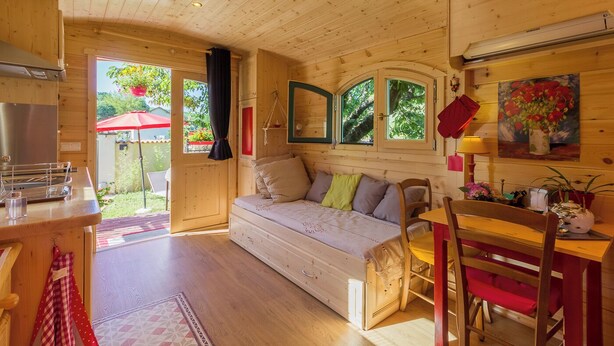 Un interior de cabaña acogedor, con suelo de madera, una cama sofá, una mesa de comedor y una zona de cocina.