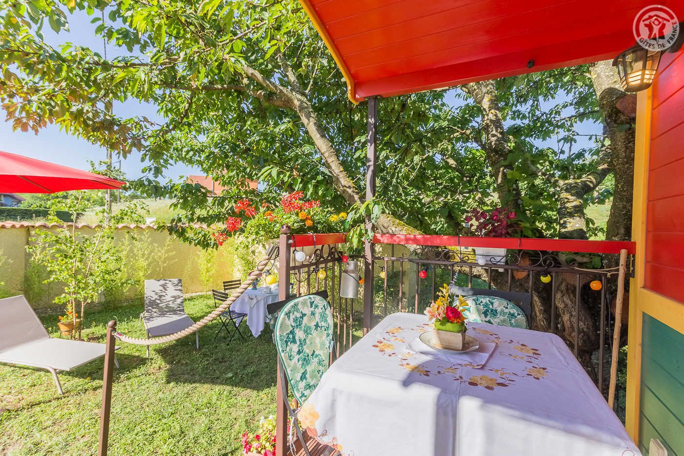 An outdoor dining area with a table set for two, surrounded by chairs and a red umbrella.