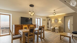 A modern living room with a dining area, wooden furniture, and a TV on the wall.