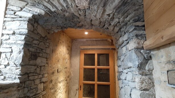 A stone archway leading to a wooden door with a window, indicating a passageway or entrance to a room.