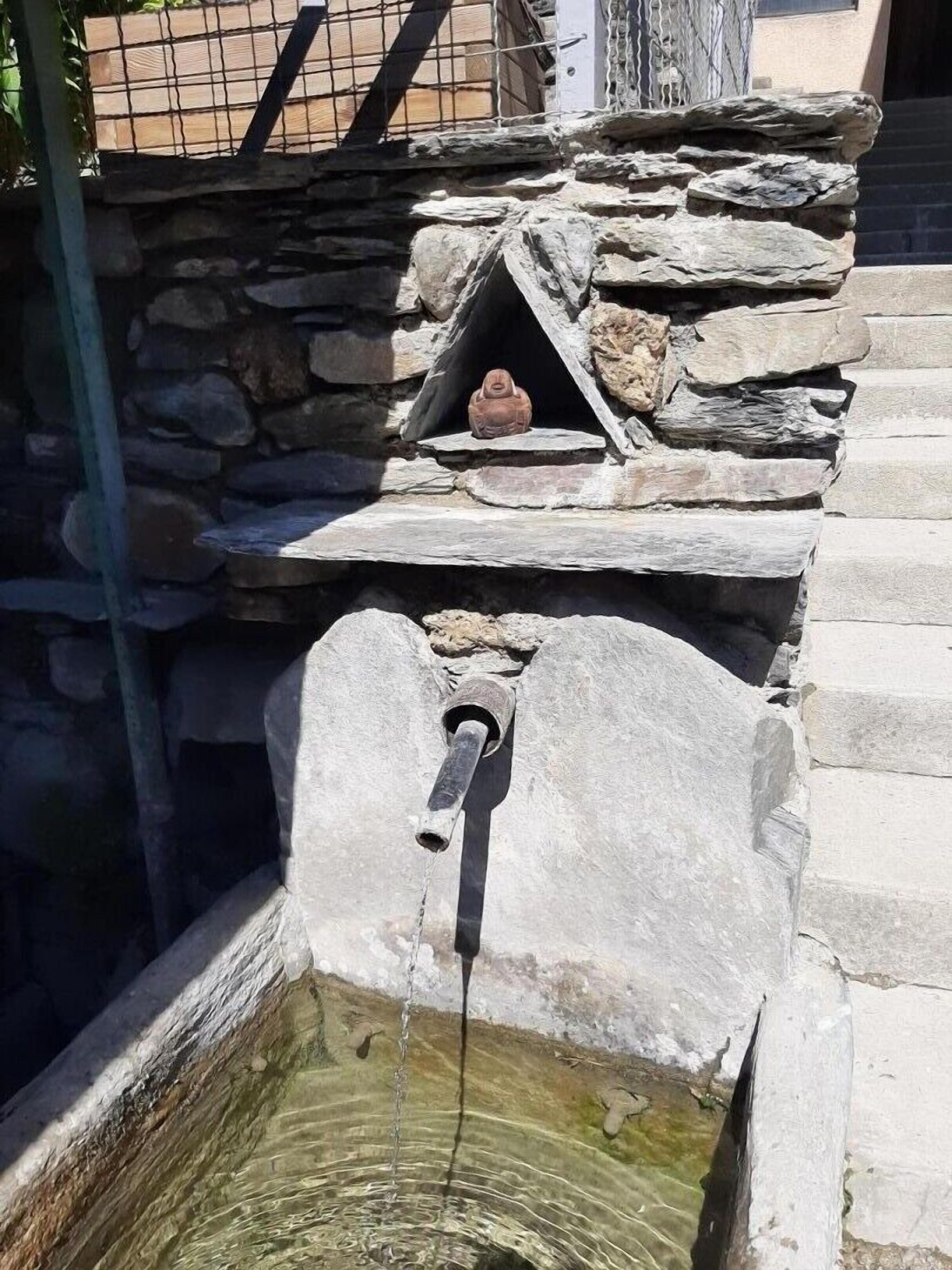 Une fontaine en pierre dotée d’un bec verseur et d’une petite étagère en pierre.