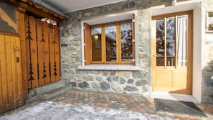 A stone building with wooden doors and windows, a stone-paved entrance, and a metal grate. - L'eglantier - Meribel-les-allues (MERIBEL LES ALLUES)
