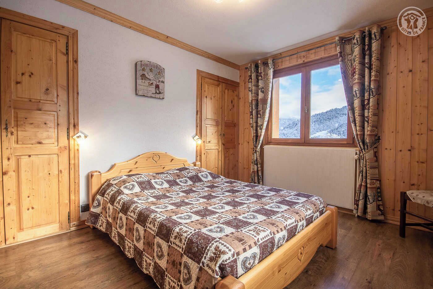 Une chambre à coucher avec un cadre en bois, un lit, une fenêtre avec des rideaux et un luminaire fixé au mur.
