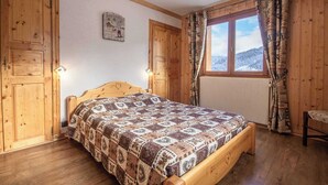 A wooden-framed bedroom with a bed, a window with curtains, and a wall-mounted light fixture. - L'eglantier - Meribel-les-allues (MERIBEL LES ALLUES)