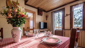 A dining area with a checkered tablecloth, a vase with flowers, and a television in the background. - L'eglantier - Meribel-les-allues (MERIBEL LES ALLUES)