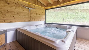 Ein Holzblockbau-Innenraum mit Whirlpool, Holzwänden und Blick durch ein Fenster auf eine Rasenfläche.