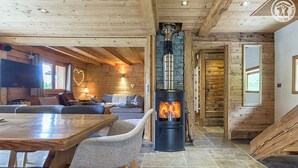 Ein gemütliches Blockhauss-Interieur mit Kamin aus Stein, Holzwänden, einem Essbereich und einem Wohnzimmer mit Sofa und Fernseher.