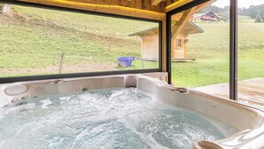 Ein Whirlpool mit Blick auf eine grüne Landschaft und eine Holzhütte.